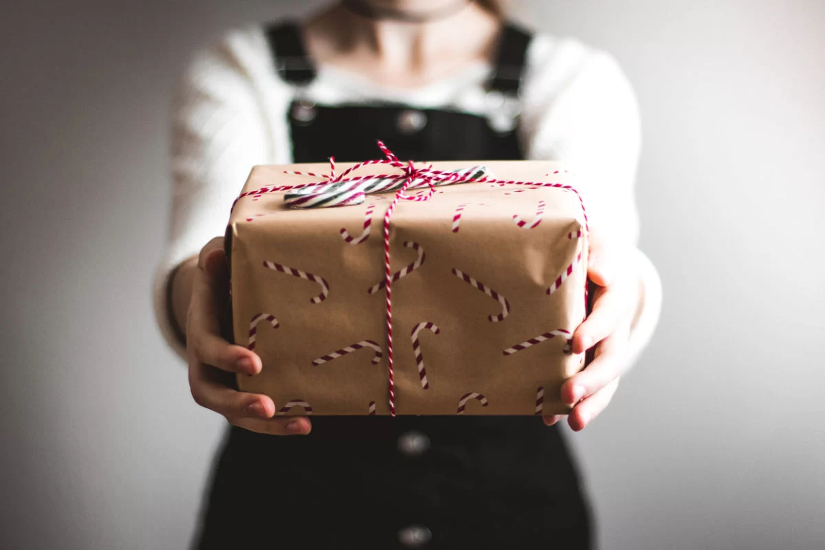 a lady holds a small christmas gift wrapped in brown paper and tied with christmas string