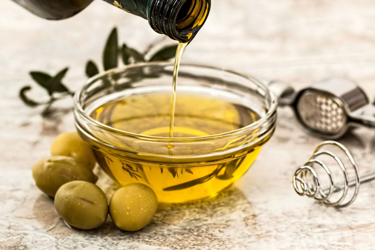 extra virgin olive oil is poured from a large bottle into a small glass bowl