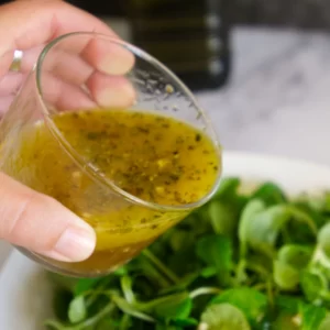 Mediterranean salad dressing in a small glass being drizzled over a green garden salad