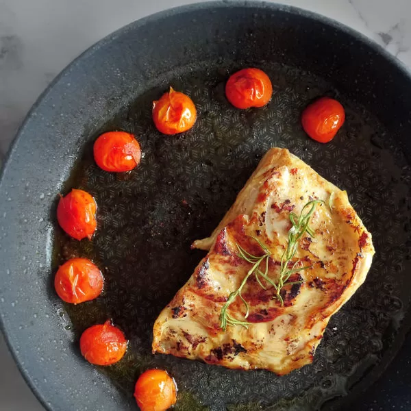 a cerdo secreto fillet sits in a frying pan dotted with fried cherry tomatoes
