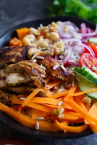 a rice bowl is topped with grilled chicken, salad, chickpeas, and a salad dressing
