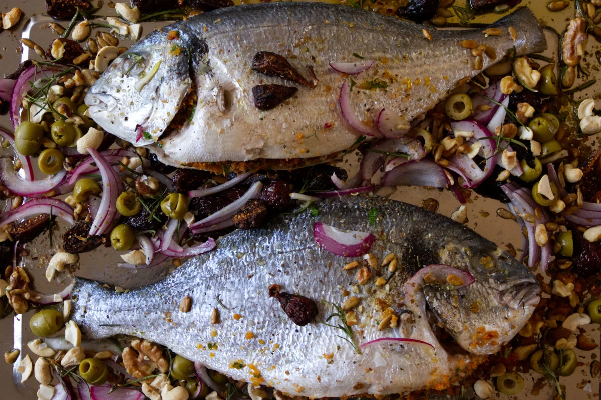 two large bream are laid out on a baking tray with lots of garnishing sprinkled over the top.