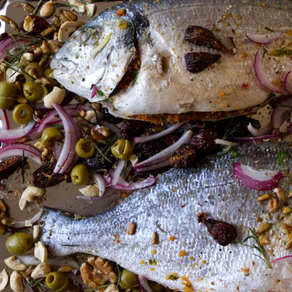 2 large whole fish sit on a baking tray with garnishing and some seasoning.