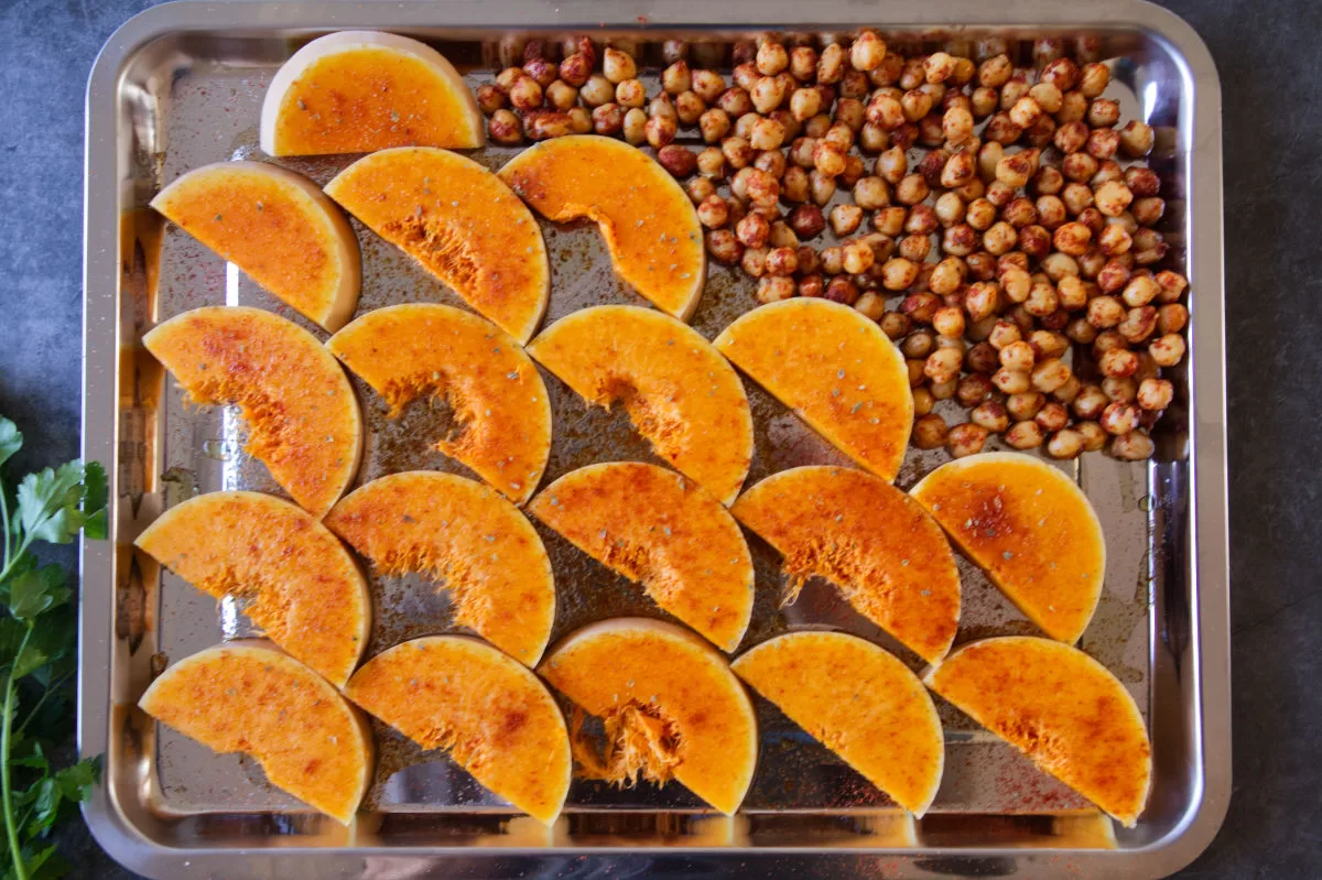 Some roasted pumpkin pieces and chickpeas sit in an oven baking tray