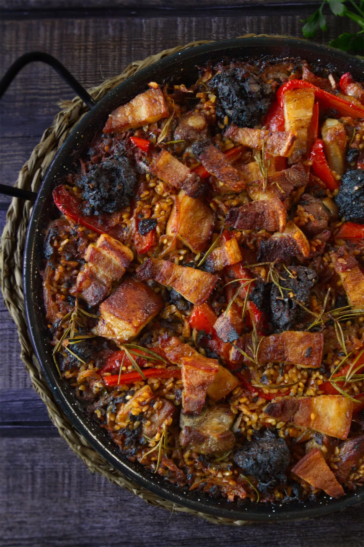 a large pan of oven baked rice is topped with lots of pancetta chunks and morcilla sausage.