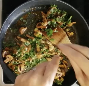 Some fresh chopped parsley is added to a pan of garlic mushrooms