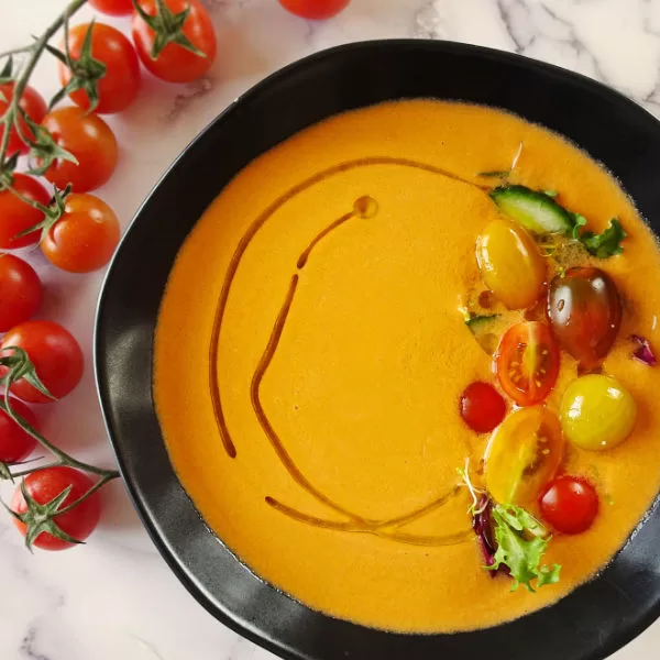 a large bowl of gazpacho andaluz sits beside some cherry tomatoes