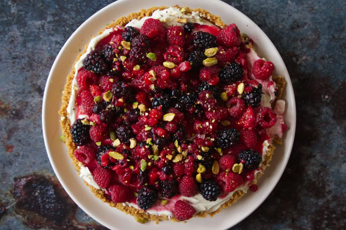 A mixed berry cheesecake sits with lots of berries on top waiting to be served.
