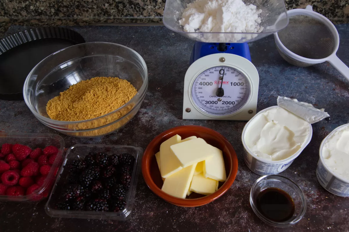 ingredients for making a mixed berry cheesecake are laid out on a kitchen counter.