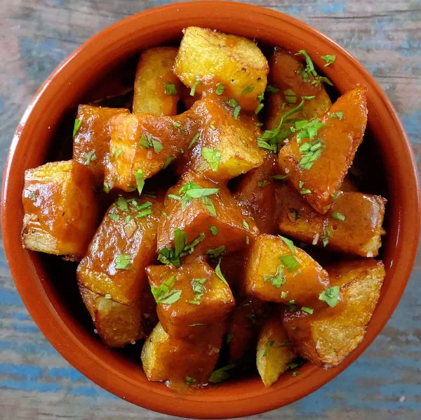 a bowl of patatas bravas sits garnished with some fresh parsley