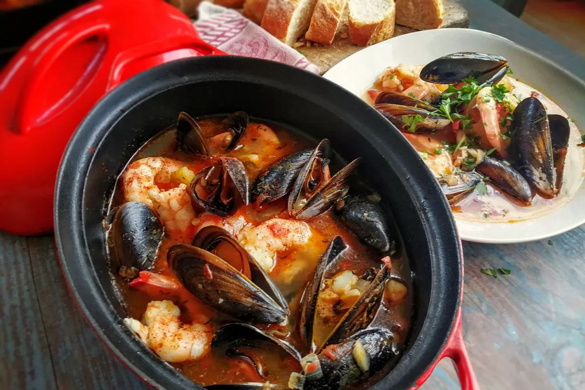 a large pot of seafood stew sits beside a bowl 