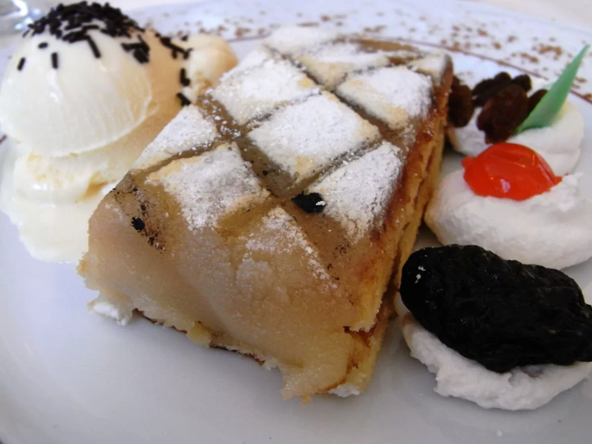 A slice of Ponche segoviano sits o a plate with some whipped cream and ice cream. 