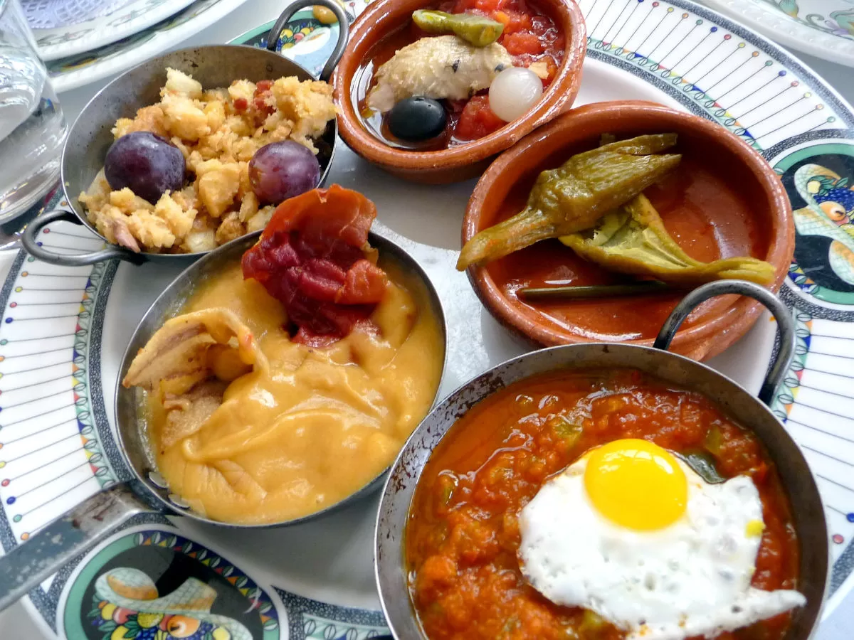 Aspread of Spanish tapas dishes are laid out on a large silver platter. 