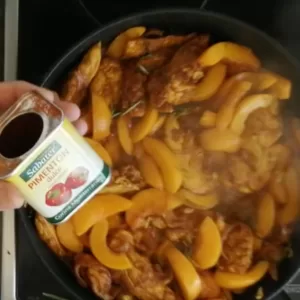 sweet paprika is added to a large pan of chicken with peaches