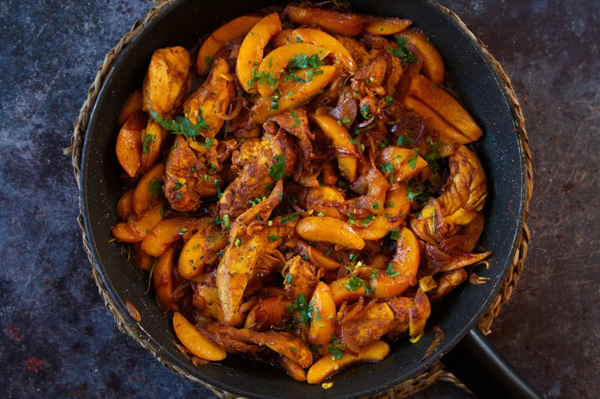 A large pan of chicken with peaches cooked in sherry.