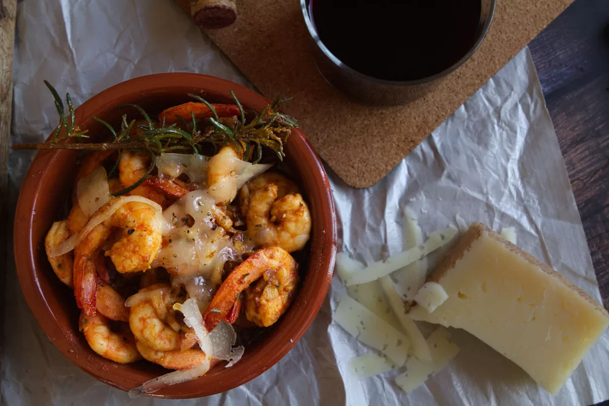 A bowl of Spanish garlic Shrimp sits beside a wedge of Manchego cheese.