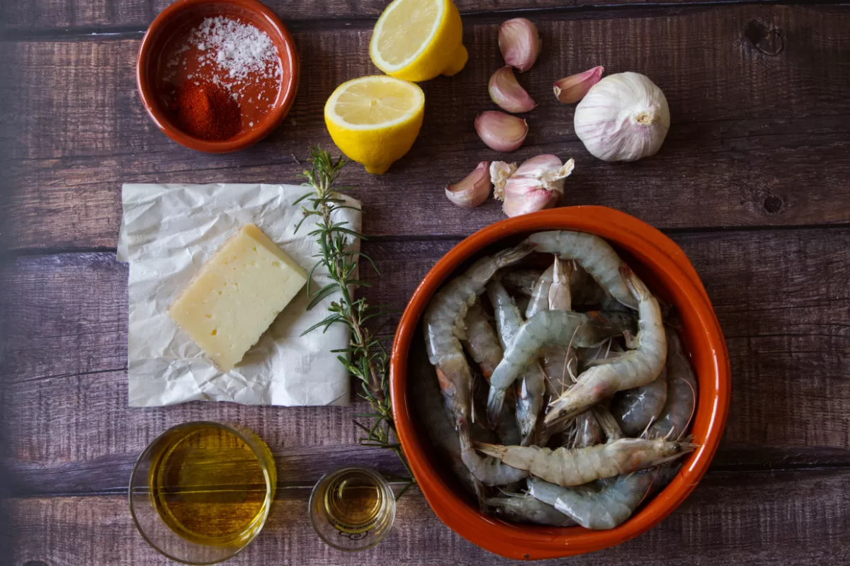 ingredients for Spanish garlic shrimp are laid out beside a large weedge of Manchego cheese.