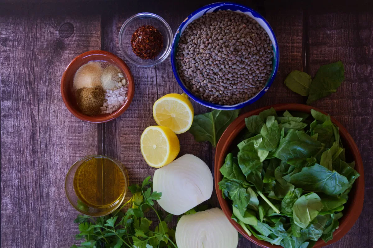 ingredients used to make Mediterranean lentil and spinach stew are laid out on a wooden counter top. 