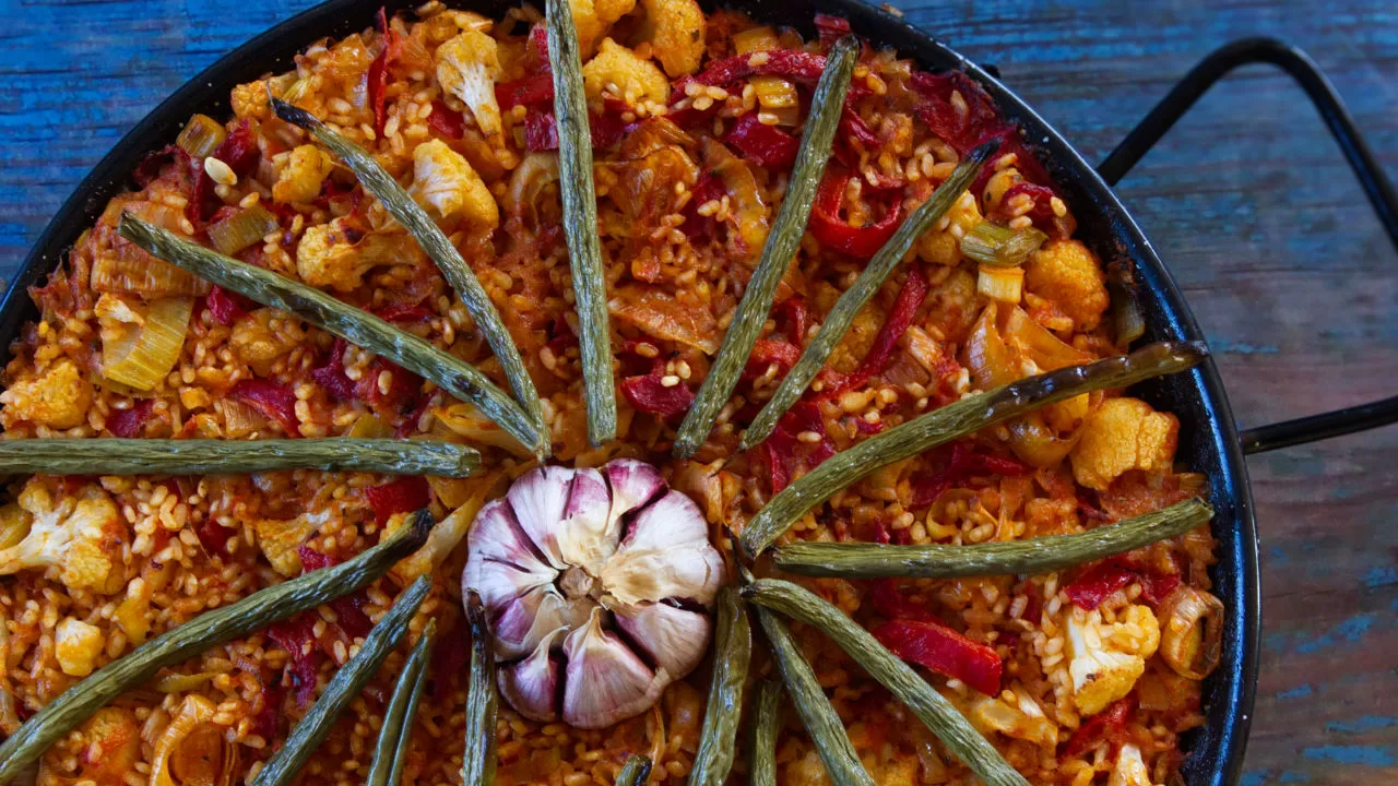 A large pan of Spanish oven-baked rice is decorated with a head of garlic and some roasted green beans