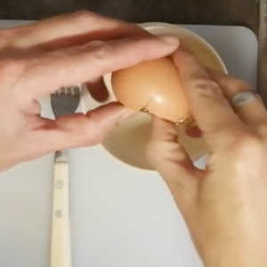 a person cracks an egg into a small bowl