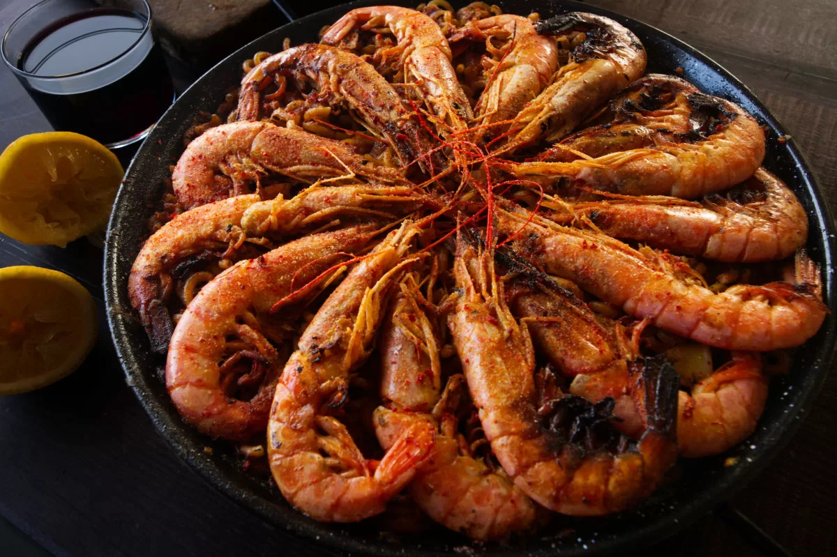 a large pan of Spanish fideua marisco is topped with lots of cooked shrimp. 