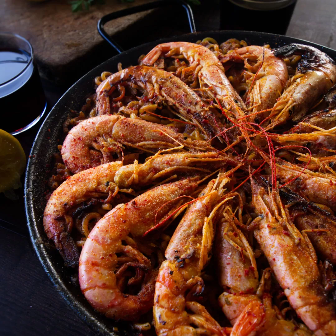 a large pan of fideua marisco sits topped with lots of large shrimp. 