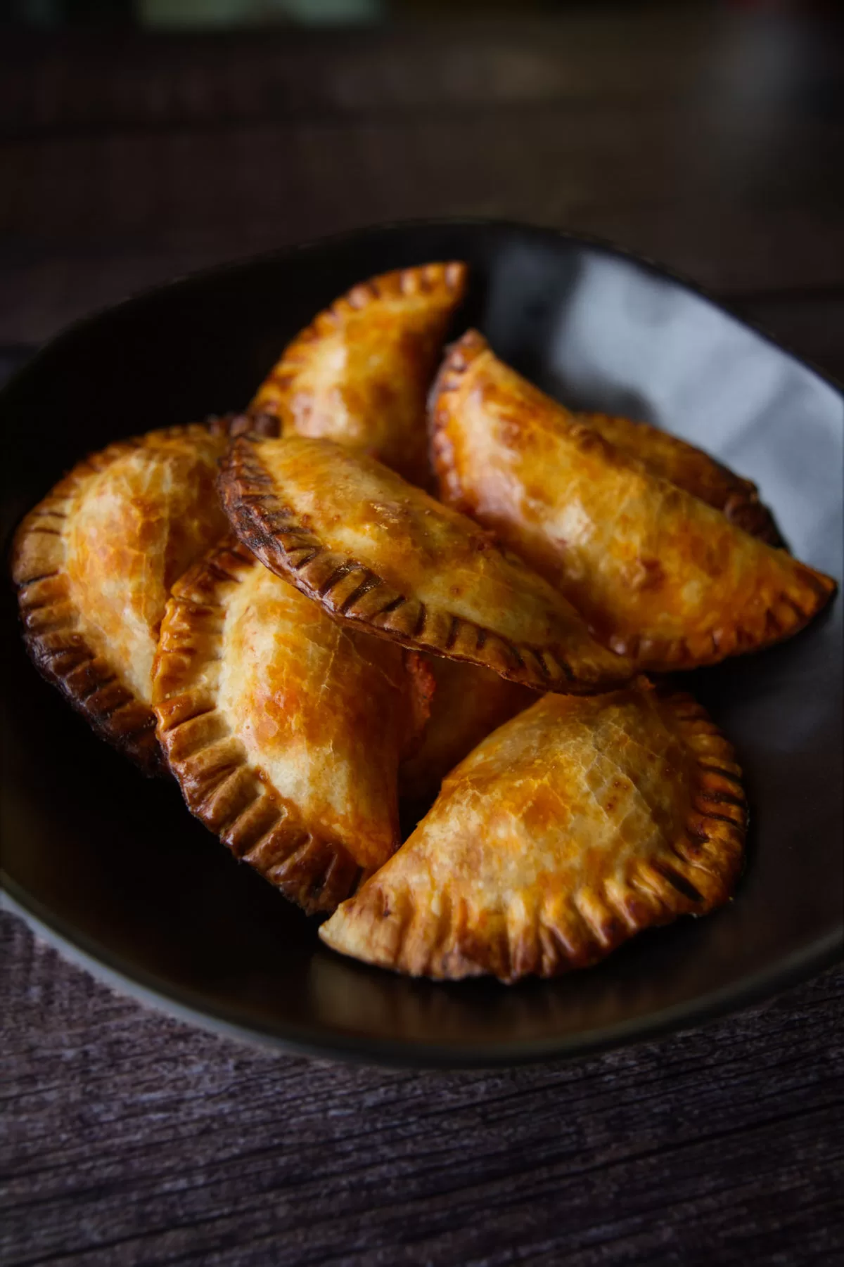 a black bowl is filled with baked empanadas with fish and romesco sauce filling.