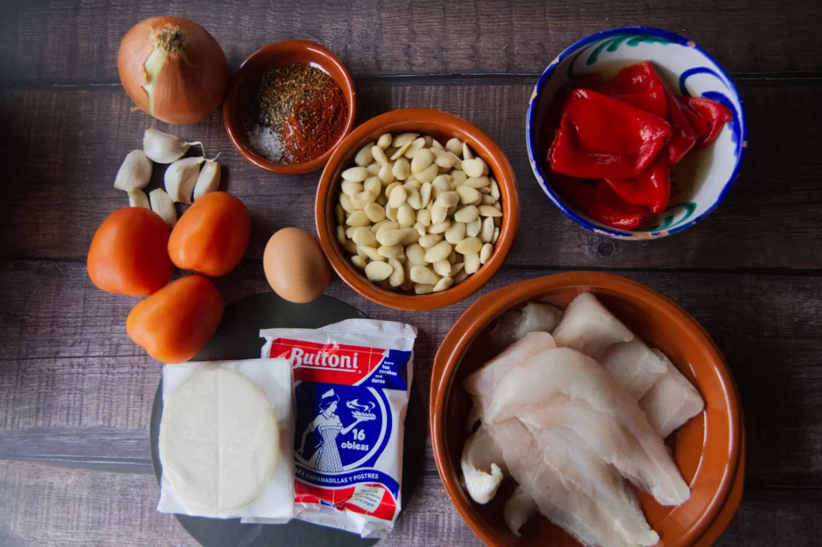 ingedients for making baked empanadas with fish and romesco sauce are laid out on a wooden countertop. 