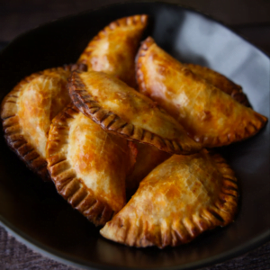 a black bowl is filled with baked empanadas.