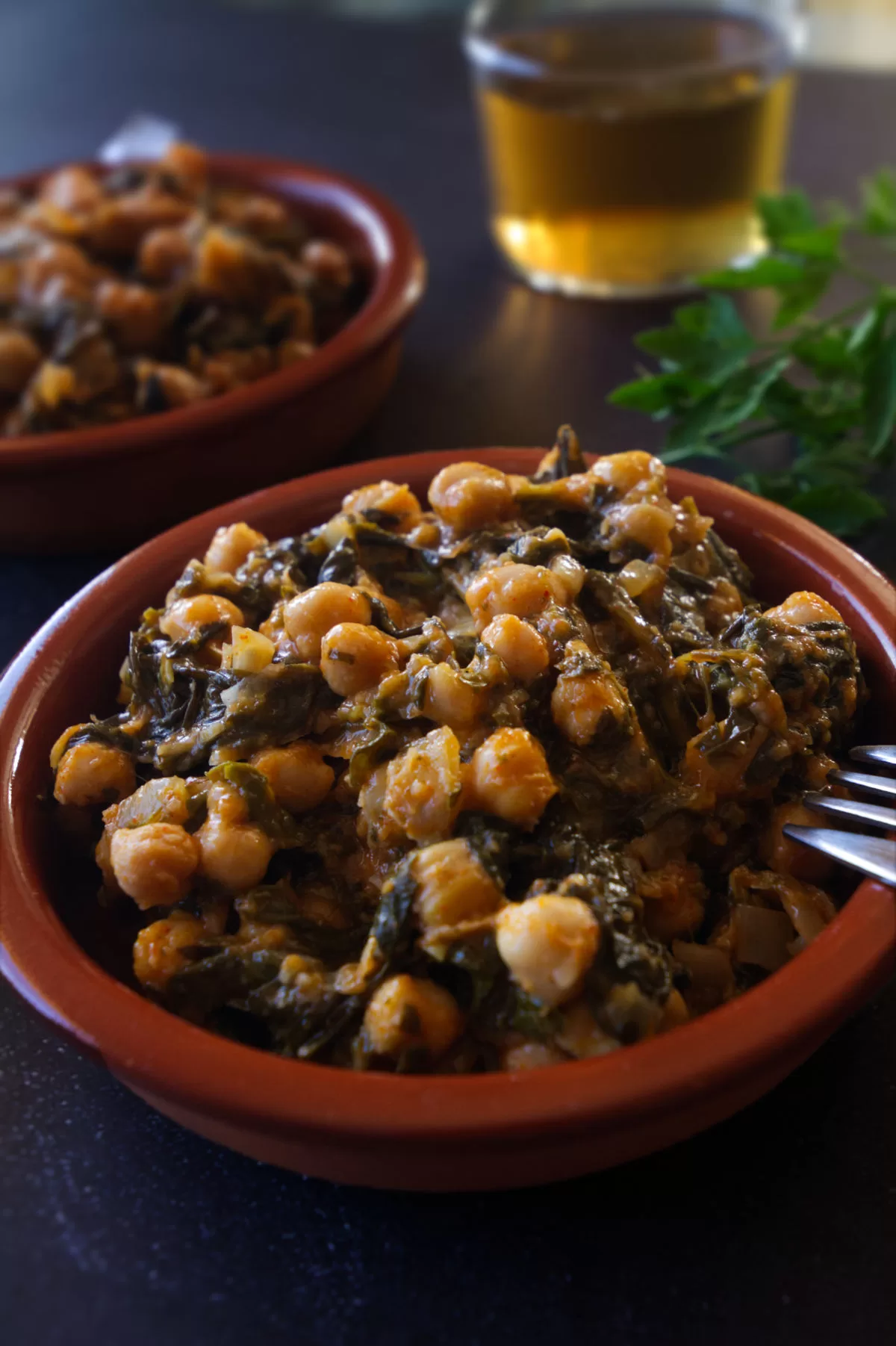 A small tapas serving of Spinach with chickpeas sits on a table beside a small glass of beer.