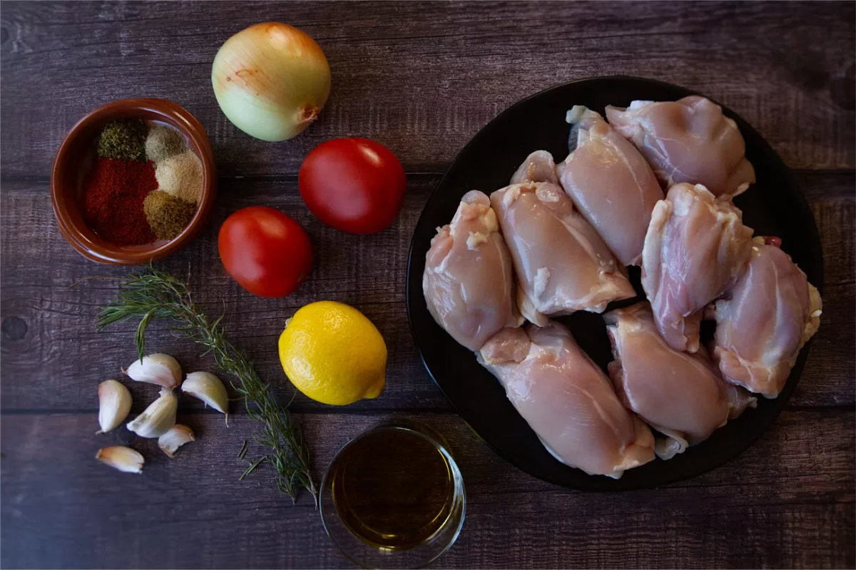 Ingredients for making baked Mediterranean chicken thighs is laid out on a table. 