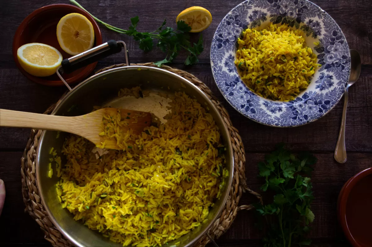 A large pot of Mediterranean yellow rice is being served to a small bowl with lemon and parsley
