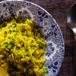 A bowl of Mediterranean yellow rice sits beside a spoon