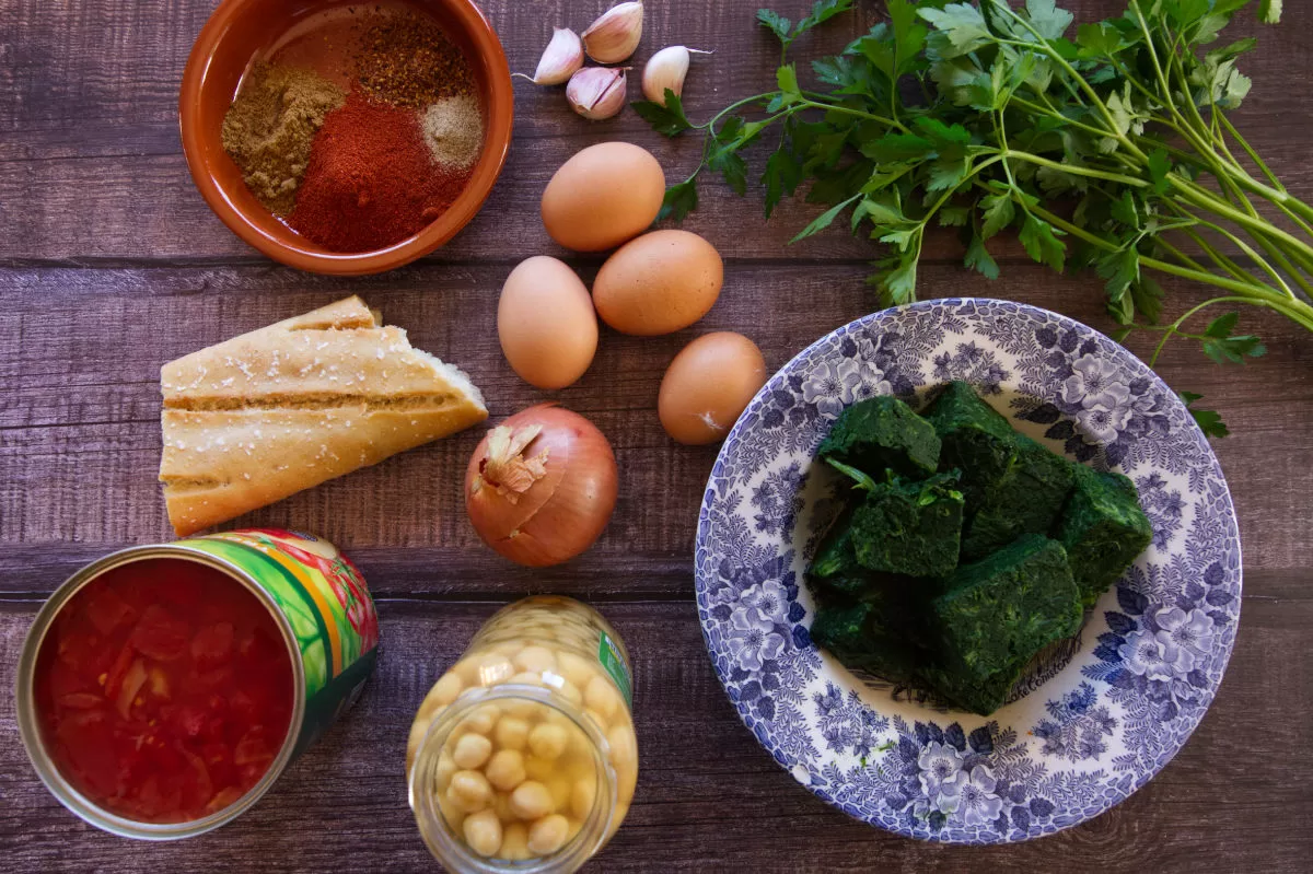 ingredients used to make chickpeas with spinach and eggs are laid out on a wodden counter.