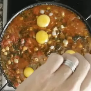 Some eggs are added to a pan of chickpeas with spinach.