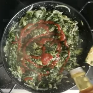 tomato sauce and vinegar are added to a pan of sauteed spinach and onions.