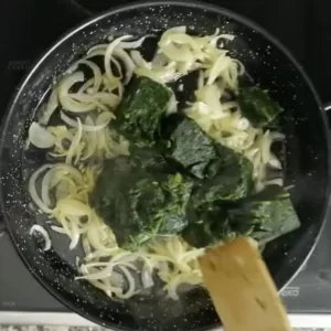 Spinach is added to a pan of sauteed onions and garlic.