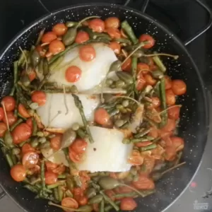 cod fillets are added to a pan of sauteed asparagus and cherry tomatoes.