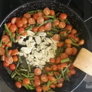 garlic is added to the pan of sauteed asparagus and tomatoes