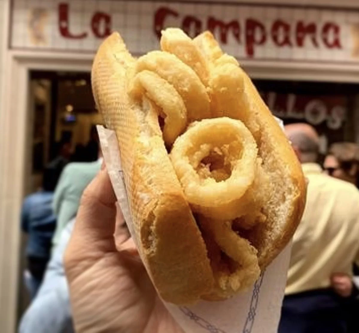 A bocadillo with calamary is help up in front of the famous restaurant La Campana in Madrid.