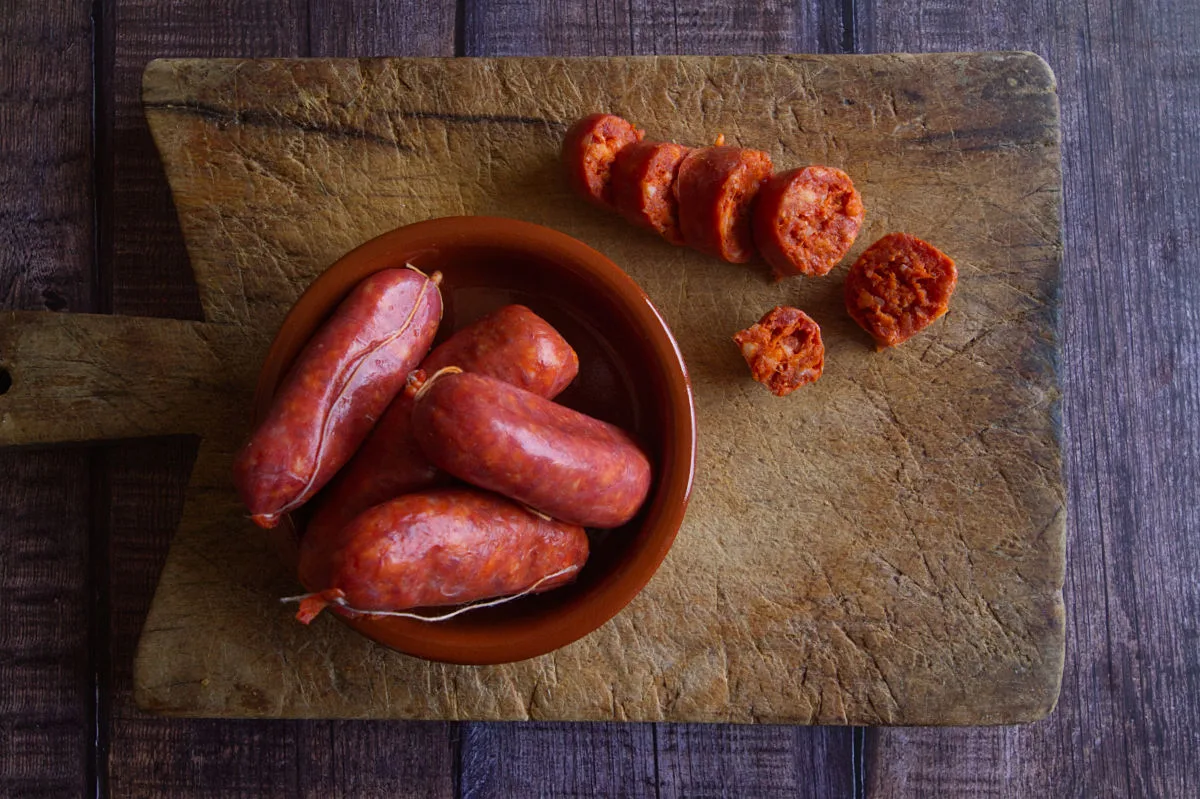 A bowl or red chorizo sausage sits next to some sliced chorizo pieces. 