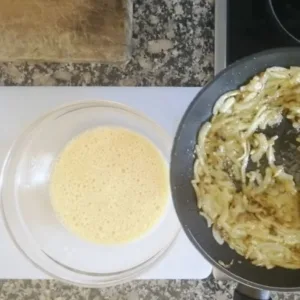 Onion is added to a bowl of wissked eggs.