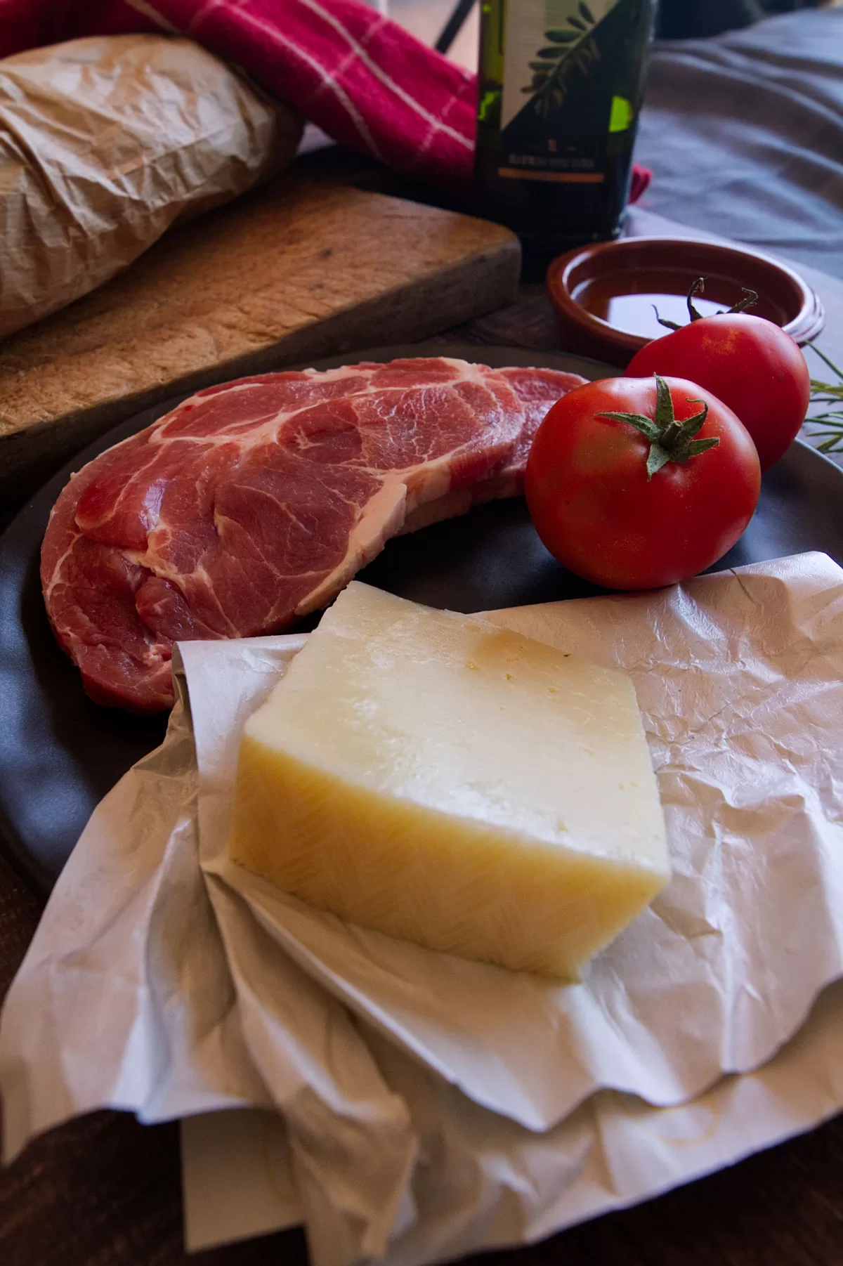 a large piece of cheese sits beside some tomatoes and slices of pork tenderloin.