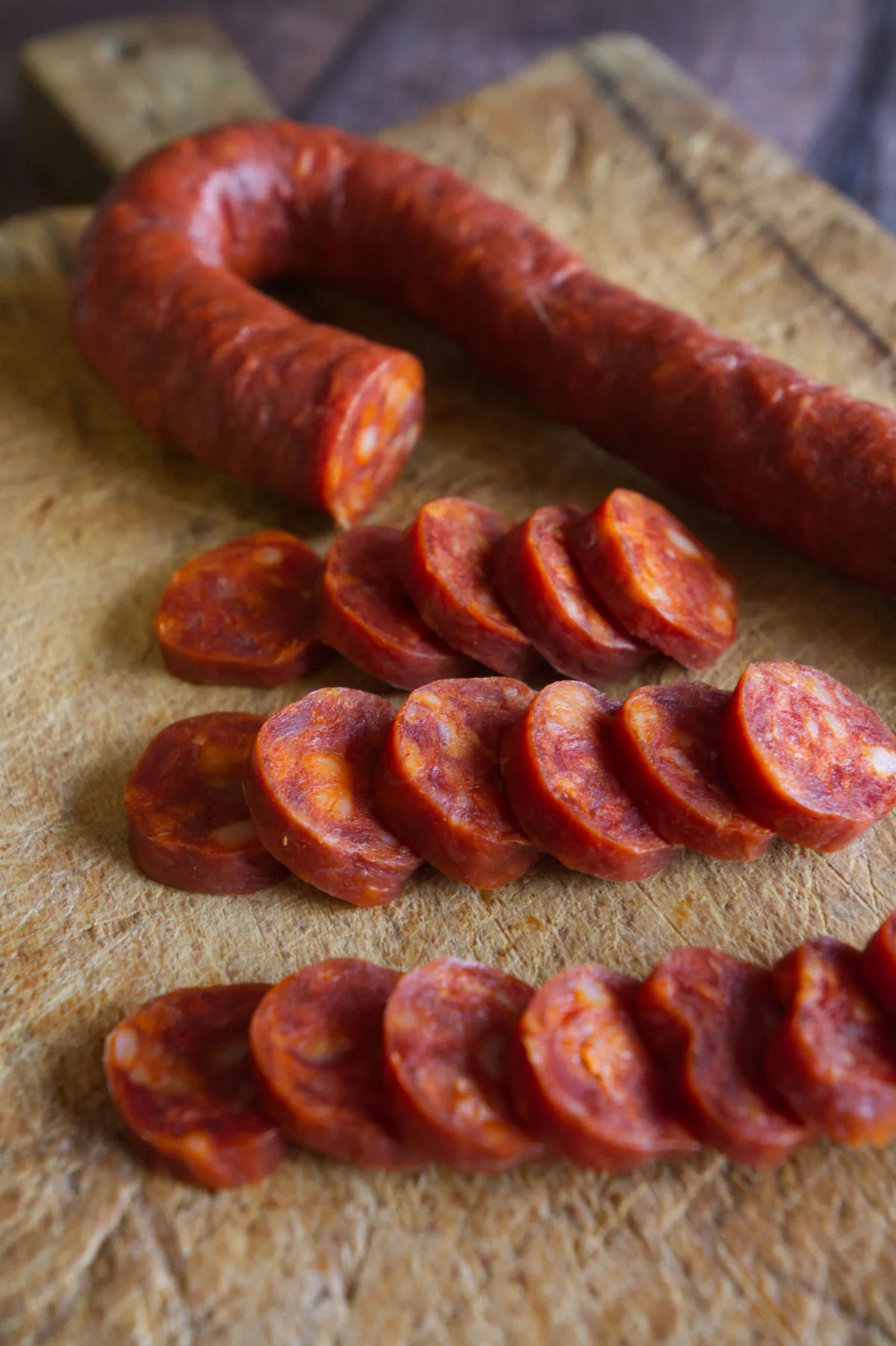 A CHOPPING BOARD WITH SOME FRESH RED CHORIZO CUT INTO SLICES. 