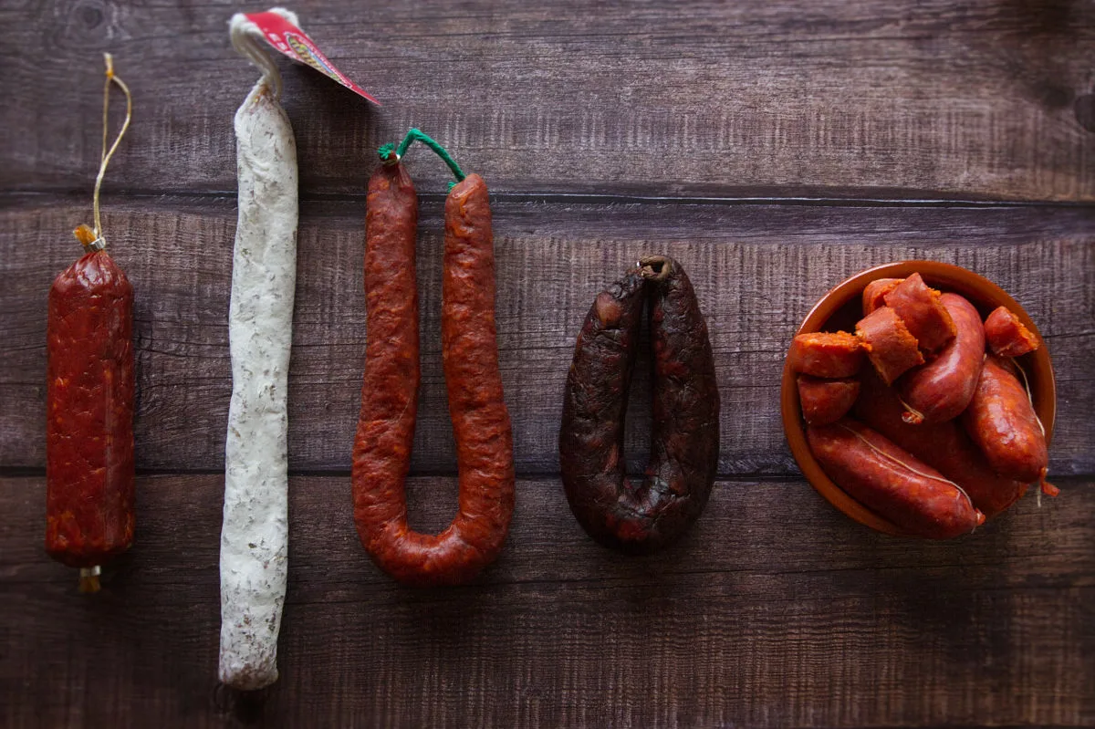 Differnt types of Spanish chorizo sit on a wooden kitchen counter. 