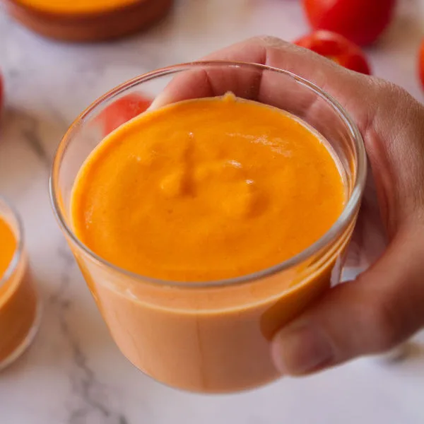 a small glass of vegan salmorejo is held by a hand
