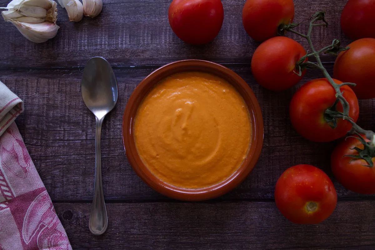 a small bowl of vegan salmorejo sits beside some on-vine tomatoes. 