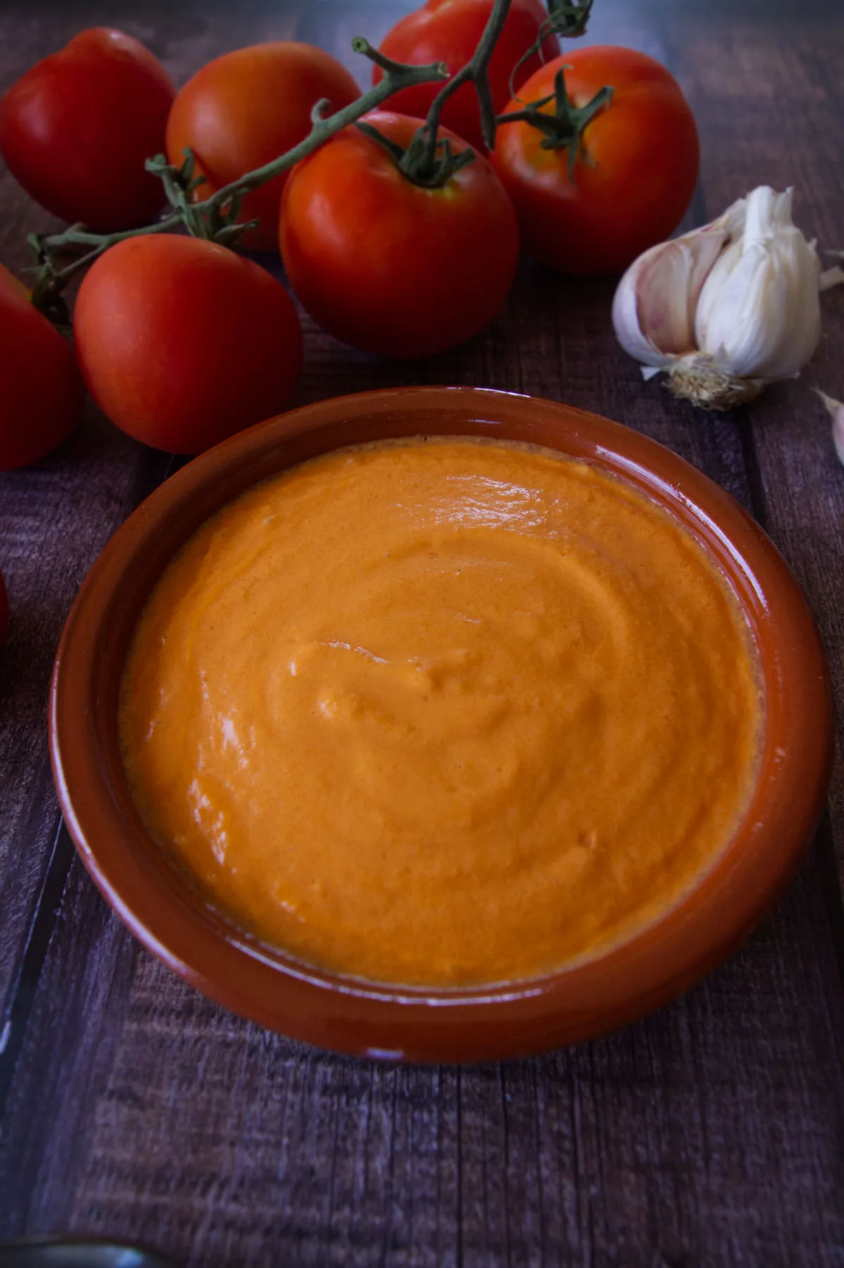 a small bowl of vegan salmorejo sits beside some on-vine tomatoes.