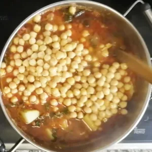 Chickpeas are added to a large pot of ingredients.