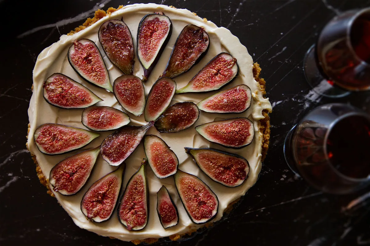 a fig and vermouth cheesecake sits beside two small glasses of vermouth on a black marble counter